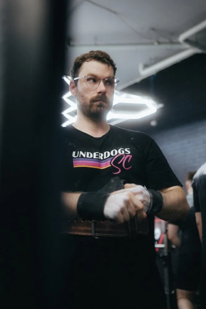 A lifter throwing both arms up in celebration after locking out a deadlift