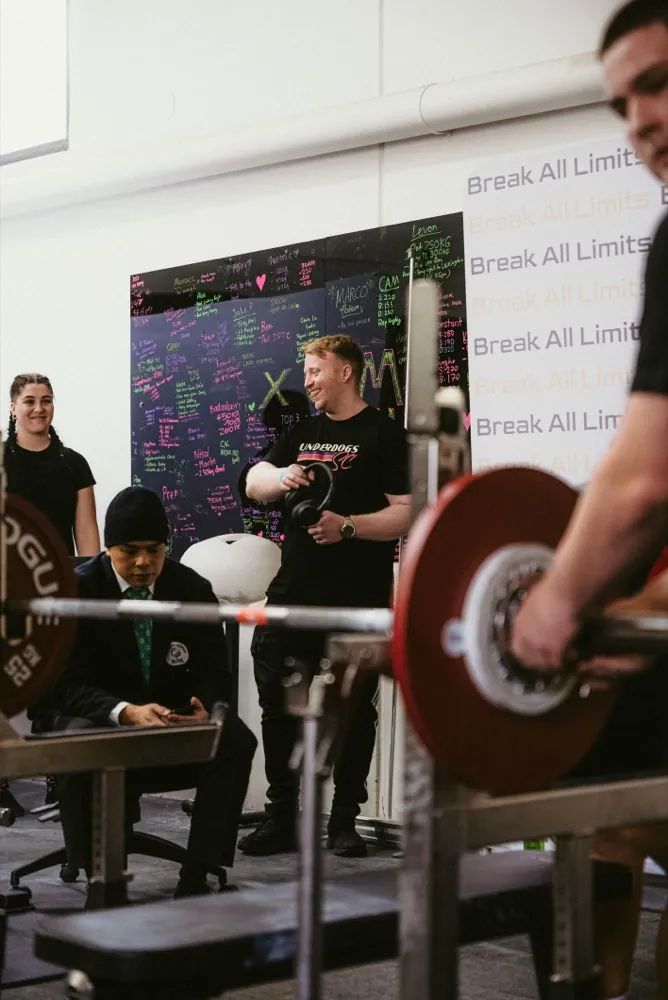 A lifter in a blue singlet locking out a heavy deadlift with a spotter behind